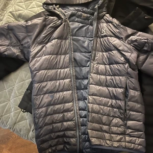 Mörkblå dunjacka från Haglöfs - Säljer en snygg och varm mörkblå dunjacka från Haglöfs. Jackan har en dragkedja feamtill. Den är lätt och smidig att bära, med en stilren design som passar till det mesta. Perfekt för både vardag och friluftsliv! Vid intresse finns fler bilder.