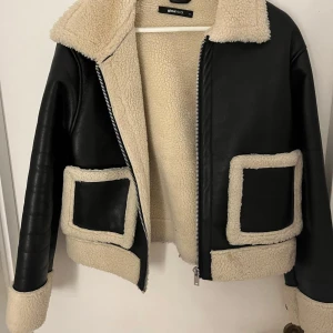 Svart skinnjacka med foder från Gina tricot  - Säljer en supercool svart skinnjacka från bikbok med mysigt beige foder. Jackan har en dragkedja framtill och stora fickor med samma foder. Perfekt för höst och vinter när du vill hålla dig varm och snygg. 