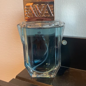 Ad Vitam Aeternam Eau de Toilette - Säljer en elegant flaska Ad Vitam Aeternam Eau de Toilette. Flaskan är stilrent designad med en klar glasflaska och en silverfärgad kork med bokstäverna AVA ingraverade. Parfymen har en fräsch blå färg och rymmer 100 ml. Perfekt för den som vill ha en tidlös doft i sin samling.