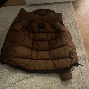 Brun dunjacka från Peak Performance - Säljer en riktigt fet, bekväm och skön vinterjacka i bra skick (7,5/10). Den har ett litet hål på ryggen och en liten fläck på framsidan, men fläcken går lätt att tvätta bort. Perfekt för kalla dagar! Kontakta mig för mer information eller bilder.