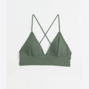 Grön ribbad topp med smala axelband - Säljer en snygg grön ribbad badbh med smala axelband som korsas i ryggen. Perfekt för sommardagar eller som ett lager under en skjorta. Toppen har en enkel och stilren design med en bred kant nedtill för extra stöd. Nypris 180kr 💚