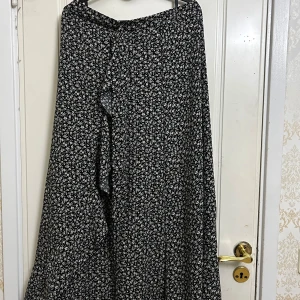Svart kjol med blommor  - Svart kjol med vita blommor perfekt till sommaren. Har en dragkedja och 2 snören man kan knyta. Använts 2 gånger. 