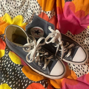 Blåa Converse sneakers - Klassiska blåa Converse sneakers med vita snören och tåhätta. Perfekta för en avslappnad stil och passar till det mesta. Hög modell med det ikoniska Converse-märket på sidan.