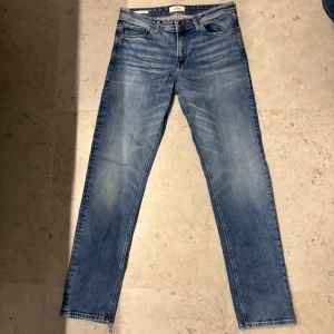 Blå jeans från Jack & Jones - Snygga blå jeans från Jack & Jones med klassisk femficksdesign och knappgylf. Perfekta för en avslappnad stil. Storlek W30 L34