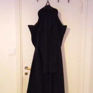 Svart kappa från Kappahl - Elegant svart kappa från Kappahl i storlek S. Tillverkad av 100% polyester, perfekt för kyligare dagar. Klassisk design med knappar framtill och en stilren siluett. Orginal pris 1000 säljs för 600.