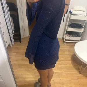Glittrig  klänning - Snygg mörkblå klänning med glitterdetaljer och öppen rygg. Klänningen har långa ärmar och en tight passform som framhäver kroppens former. Perfekt för en kväll ute! 