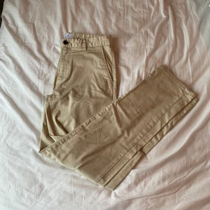 Beige byxor från Les Deux - Snygga beige byxor från Les Deux, perfekta för en stilren look. Byxorna har en klassisk design med raka ben och diskreta bakfickor. Tillverkade i Turkiet, dessa byxor är både bekväma och eleganta.