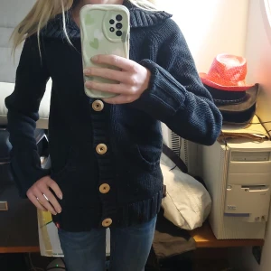 Svart vintage stickad kofta med knappar -  Trendig svart stickad kofta med stora träknappar framtill.  Krage längre upp till och ärmarna går att vika upp. Skulle säga att den kan passa storlek XS till M