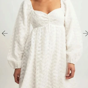 Vit klänning med puffärmar - Säljer denna otroligt söta, fina och populära miniklänningen från NA-KD i storlek 36. Den är långärmad med lite vadderade axlar, har en hjärtformad urringning och är dubbel fodrad. Klänningen är fylld med små söta blommor. Perfekt för bl.a. studenten. Använd endast 1 gång!!