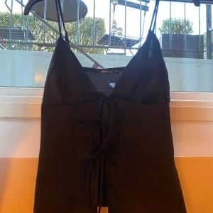 Svart linnetopp från Gina Tricot - Snygg svart linnetopp från Gina Tricot med smala axelband och knytning framtill. Perfekt som festtopp vid varmare tillfällen! Skulle säga att den passar en XS mer än en S på grund av knytningen över bysten.