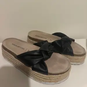 Snygga svarta sandaler med en dekorativ rosett på ovansidan. Sandalerna har en platåsula i naturmaterial som ger en somrig känsla. Perfekta för varma dagar.