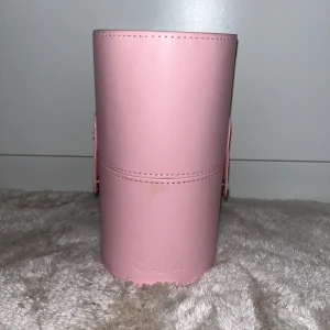 Rosa sminkborstfodral från Caia - Snyggt rosa sminkborstfodral från Caia, perfekt för att förvara dina sminkborstar. Fodralet är cylinderformat och har en praktisk stängning. Perfekt för resor eller att hålla ordning hemma.