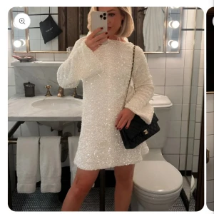 Vit glittrig klänning med öppen rygg ( bild tagen från hemsidan)  - Snygg vit glittrig klänning med lång ärm och en elegant öppen rygg. Klänningen har en stor svart rosett baktill som ger en extra touch av glamour. Perfekt för en festlig kväll!  Helt oanvänd, endast testad och har kvar prislappen. Skriv för mer bilder. Original pris 1045 kr säljer för 500 