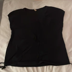 Svart topp från Soyaconcept - Snygg svart topp från Soyaconcept i storlek S. Toppen har en enkel design med korta ärmar och knytband i nederkanten för en justerbar passform. Perfekt för en stilren look.