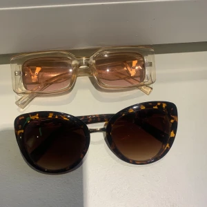 Två par solglasögon - Två par solglasögon: ett par med rektangulära, transparenta bågar och rosa tonade glas, samt ett par med kattögonformade bågar i leopardmönster och mörka glas.