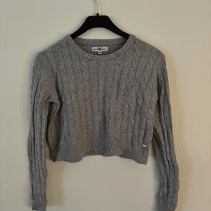 Grå stickad tröja från Hampton Republic - Säljer en stilren grå stickad tröja från Hampton Republic. Tröjan har ett klassiskt flätmönster med långa ärmar. Perfekt för alla tillfällen! 