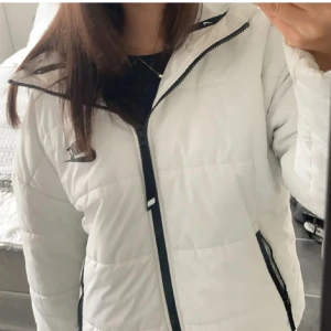 Vit pufferjacka från Nike - Säljer en snygg vit pufferjacka från Nike med svart dragkedja och logga. Jackan har en huva och långa ärmar, perfekt för kyliga dagar. Den har en sportig look och är både stilren och bekväm. Nypriset låg runt 1200kr💕💕