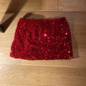 Röd paljettkjol från Lindex - Snygg röd paljettkjol från Lindex i storlek 152/164. Perfekt för att glittra på festen med sin korta längd och iögonfallande design. Kjolen är täckt av röda paljetter som ger en glamorös look.