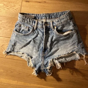 Blå jeansshorts från Zara - Säljer ett par coola blå jeansshorts från Zara.  med slitna kanter och klassisk femficksdesign. Perfekta för en avslappnad sommarlook!