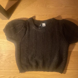 Svart stickad tröja från Divided - Säljer en svart stickad tröja från Divided med korta puffärmar och ett fint stickat mönster. Tröjan har ribbstickade kanter vid ärmslut och nederkant. Och har aldrig användas 