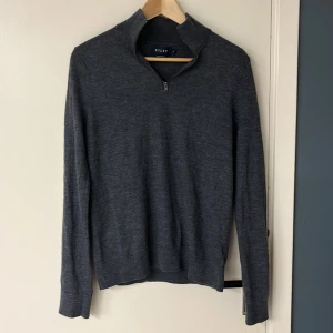 Grå merinoulltröja från Riley - Säljer en stilren grå tröja från Riley i mjuk merinoull. Tröjan har en halv dragkedja och långa ärmar, perfekt för kyligare dagar. Passar både till vardags och mer uppklädda tillfällen. Skick 8/10