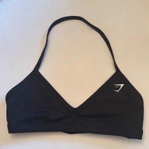 Svart sport-bh från Gymshark - Snygg svart sport-bh från Gymshark med v-ringad design. Perfekt för både träning och bad. Enkel och stilren med en liten logga på framsidan.