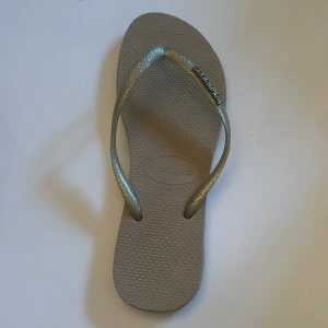 Beige flip-flops från Havaianas - Snygga och bekväma flip-flops från Havaianas i beige med glittriga remmar. Perfekta för sommardagar på stranden eller i stan. Lätta att matcha med olika outfits.