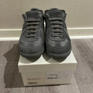 Grå sneakers från Maison Margiela - Snygga grå sneakers från Maison Margiela med en stilren design. Skorna har snörning och är tillverkade i en kombination av mocka och skinn.  Hör av er vid minsta fundering.