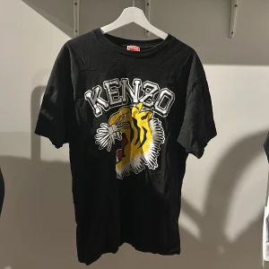 Kenzo Paris t-shirt - Säljer denna svarta t shirt från ”kenzo Paris” med den klassiska tiger logan. Köptes i nk Göteborg för cirka ett år sedan. På bilden är den ej tvättad och har legat i en garderob ganska länge därför ser den lite skrinklig ut. Nypris är 1799kr.skick 9/10 Den är i storlek medium men lite oversized passform. Har tagsen kvar. Hör av dig!