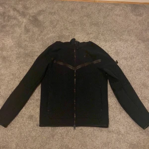 Svart fleecejacka från Nike - Säljer en svart fleecejacka från Nike med dragkedja framtill. Jackan har en stilren design med långa ärmar och hög krage. Perfekt för kyliga dagar.