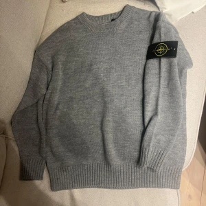 Unik Grå stickad tröja från Stone Island - Säljer min helt nya grå stickade tröja från Stone Island med deras ikoniska märke på ärmen. Tröjan var för liten för mig som e 185 o därför säljer jag den. Den e skön och sticks ej och är gjord i ett tjockt material. Tveka inte på o skriv då det behövs göras av med! Inget äktighets bevis