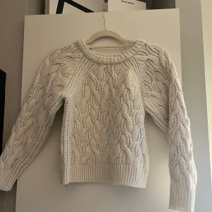 Benvit stickad tröja med flätmönster - Benvit flätstickad tröja, tröjan har en viten tråd som hänger på ena armen men den kan man bara klippa av.