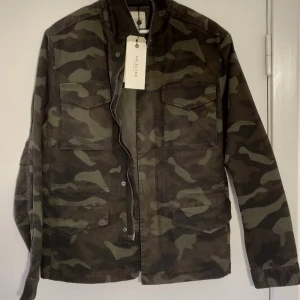 Camouflagejacka från Selected Homme - Snygg camouflagejacka från Selected Homme i storlek M. Jackan har en dragkedja och flera praktiska fickor framtill. Perfekt för en cool och avslappnad stil. orginalpriset var 1600  SEK 