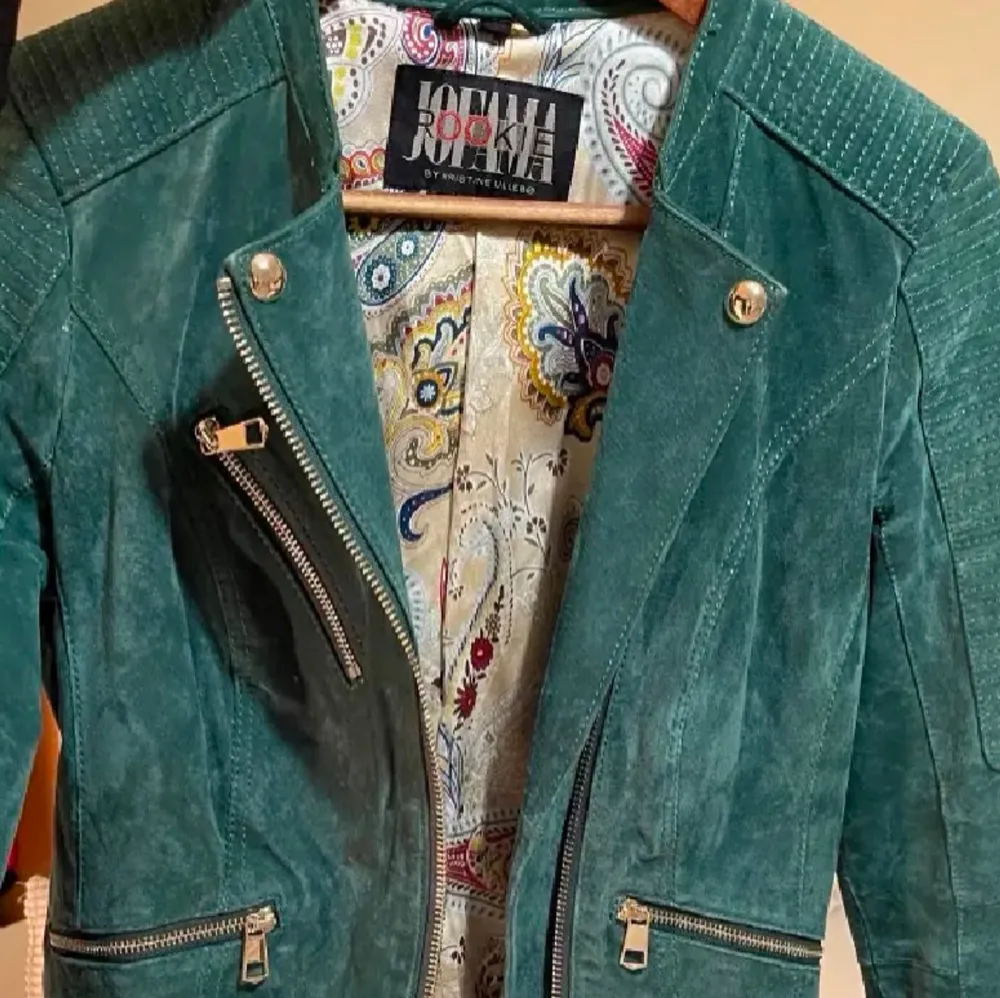 Snygg grön mockajacka från Jofama med asymmetrisk dragkedja och flera fickor med dragkedjor. Jackan har quiltade detaljer på axlarna och ett färgglatt mönstrat foder 💚. Takit.