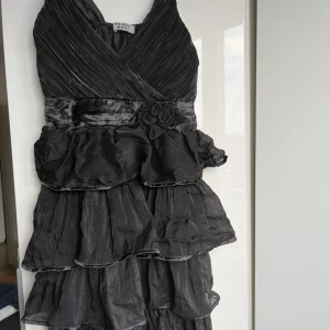 Svart klänning från Yajula Moda - Svart klänning med volanger och rosett detalj framtill, har själv bara använt den en gång! Klänningen är något skrimrigt vilket kan ses i olika ljus, annars svart. Som Ref är jag ca 160 och längden är till mina lår 