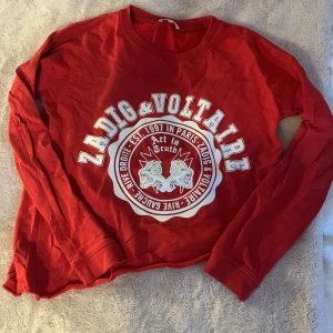 Röd långärmad tröja från Zadig & Voltaire - Snygg röd långärmad tröja från Zadig & Voltaire med stort tryck framtill. Perfekt för en avslappnad stil med en touch av rock'n'roll. Tröjan har en rund halsringning och är tillverkad i mjukt material.❤️