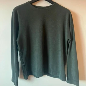 Grågrön tjocktröja från The North Face - Säljer en stilren grågrön tröja från The North Face i storlek S. Tröjan är tillverkad i polyester och har långa ärmar. Använd men har inga synliga defekter. 
