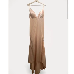 Champagnefärgad långklänning från Hebeos - Elegant champagnefärgad långklänning i vävd satin från Hebeos. Klänningen har smala axelband och en v-ringad design som ger en sofistikerad look. Perfekt för speciella tillfällen.