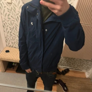 Blå peak Performance Jacka - Säljer en stilren blå Peak Performance jacka med dragkedja och knappar. Köptes för 1300kr. Använd tre gånger. Perfekt för en casual look, våren och hösten. 