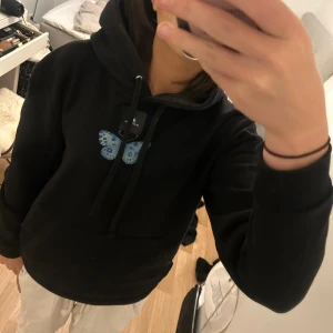 Svart hoodie med blå fjäril - Säljer en svart hoodie med en stor blå fjäril på ryggen och en mindre fjäril på framsidan. Den är supermjuk och perfekt för höst och vinter. Har en skön passform och är i nyskick. Perfekt för att mysa i eller ha på sig till vardags!