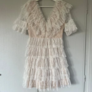 Vit spetsklänning med volanger - Säljer min superfin vit By Malina spetsklänning med volanger. Den har korta ärmar och en v-ringad design. Perfekt för studenten eller sommar fester . Klänningen är endast använda en gång 