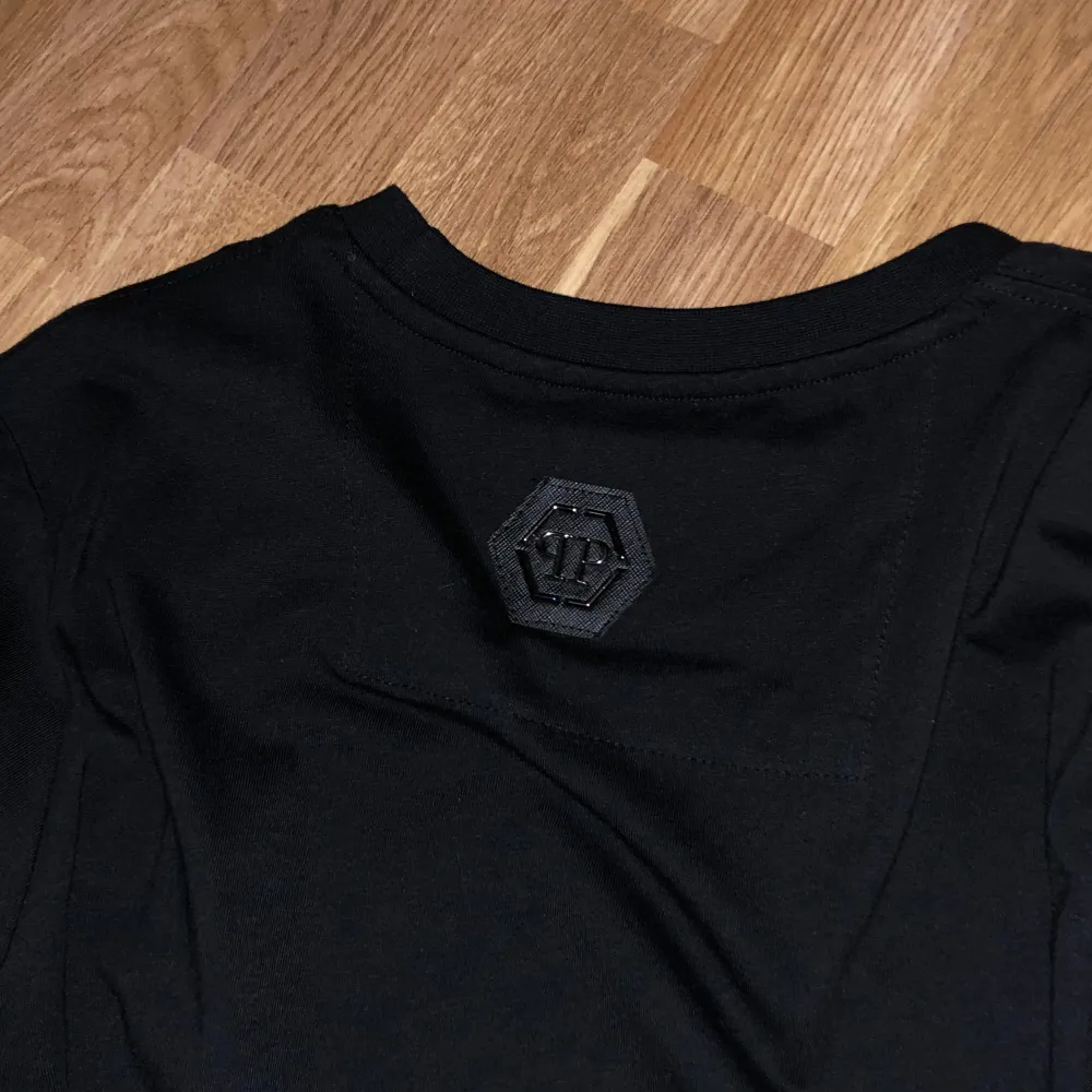 Säljer en svart t-shirt från Philipp Plein med en cool dödskalle-design i rött och vitt på framsidan. T-shirten är kortärmad och har en normal passform. Perfekt för en avslappnad stil.. T-shirts.