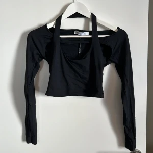 Svart croppad topp från Bershka - Säljer en svart croppad topp från Bershka. Den har en unik design med långa ärmar och en öppen axelstil. Perfekt för en utekväll eller fest! Toppen är i bra skick och redo för nya äventyr.