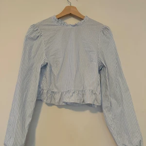 H&m Divided blåvit topp, storlek S - En blåvit randig topp med långa ärmar och en volang vid nederkanten. Toppen är i en crop-modell och har en rund halsringning.  Nypris: 149 kr  Använd 1 gång