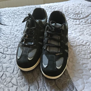 Svarta sneakers med vit sula - Säljer ett par svart/gråa sneakers med vit sula. De har en sportig design med snörning och är i ett bra skick. Skorna har svarta och grå detaljer och ser ut att vara bekväma för vardagsbruk.