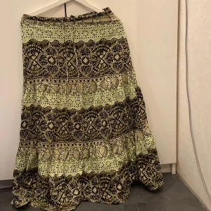 Mönstrad långkjol i grönt och brunt - Säljer en superfin långkjol med ett unikt mönster i grönt och brunt. Kjolen har en bekväm passform med elastisk midja och dragkedja. Perfekt för både vardag och festliga tillfällen. Materialet känns mjukt och skönt mot huden.