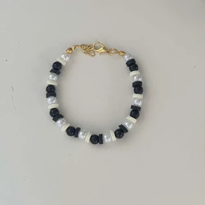 Armband med svarta och vita pärlor - Snyggt armband med en mix av svarta och vita pärlor. Armbandet har en guldfärgad kedja och lås, vilket ger en elegant touch. Perfekt för att piffa upp vilken outfit som helst!