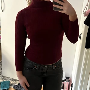 Vinröd ribbad polotröja - Säljer en snygg vinröd polotröja med ribbad struktur. Tröjan är långärmad och har en tight passform som sitter perfekt för höst och vinter. 