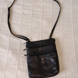 Svart skinnväska - Feel Accessories  - Svart väska i skinn/läder från Feel. Längden på axelremmen går att justera. Flera bra fack med dragkedja. Skinnet är lite slitet på några ställen. Se bilder. 