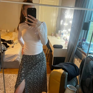 Svartvit blommig kjol med slits - Säljer en superfin svartvit blommig kjol med en snygg slits framtill. Kjolen är perfekt för både vardag och fest och har en skön passform. Den är i ett lätt och luftigt material, vilket gör den idealisk för vår och sommar. Passar perfekt med en enkel topp eller en stickad tröja för kyligare dagar.